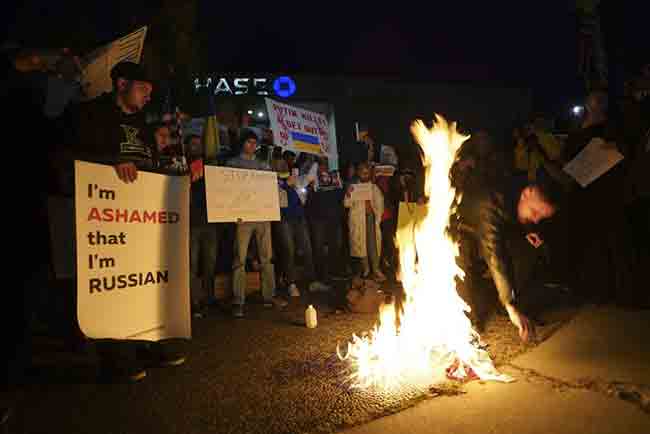 A Russian citizen burns a Russian flag as people protest the Russian invasion of Ukraine at a demonstration in the Studio City neighborhood of Los Angeles, Thursday, Feb. 24, 2022. (AP Photo/Damian Dovarganes)