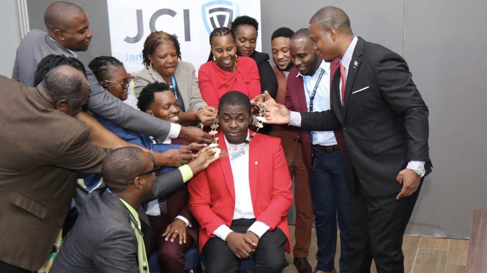CHAINED: Past presidents of Junior Chamber International (JCI) jointly places the Presidential chain on Dr. Farin Williams (seated) after he was elected as the new JCI National President. During JCI Jamaica annual convention at the Grand Palladium Resort & Spa in Lucea, Hanover on Sunday, October 4. He will assume office on January 1, 2027. – Photo Derrick Scott