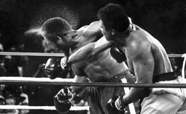 Perspiration flies from the head of George Foreman as he takes a right from challenger Muhammad Ali in the seventh round in the match dubbed Rumble in the Jungle in Kinshasa, Zaire, Oct. 30, 1974. (AP Photo/Ed Kolenovsky, File)