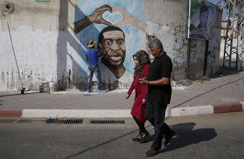 FILE - Palestinians people walk past an artist painting a mural of George Floyd, a black American who died after being restrained by police officers, in Gaza City, Tuesday, June 16, 2020. A growing number of Black Americans see the struggle of Palestinians reflected in their own fights for freedom and civil rights. In recent years, the rise of protest movements in the U.S. against police brutality in the U.S., where structural racism plagues nearly every facet of life, has connected Black and Palestinian activists under a common cause. But that kinship sometimes strains the alliance between Black and Jewish activists, which extends back several decades. (AP Photo/Hatem Moussa, File)