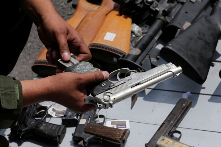 A Mexican soldier holds up a gun next to other weapons seized from alleged drug traffickers or handed in by residents before they are destroyed at a military zone in Mexico City, Mexico. [Henry Romero/Reuters]