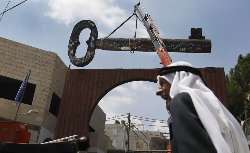 FILE - Palestinians display a huge key, known as “the Key of Return,” which was exhibited at the Berlin Biennale in March 2012, in the West Bank refugee camp of Aida near Bethlehem, Aug. 29. (AP Photo/Nasser Shiyoukhi, File)