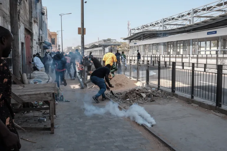 Protesters run away as a smoke grenade lands near them during clashes with police in Dakar [Guy Peterson/AFP]